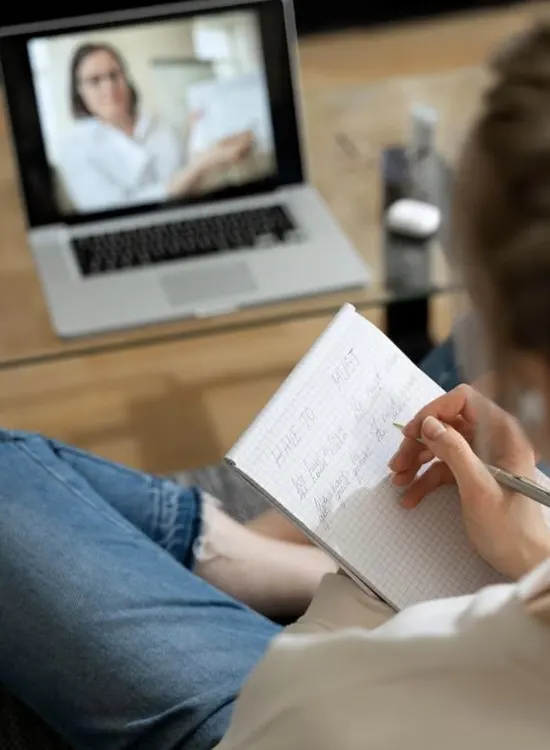 Person taking notes during a video call on a laptop screen.