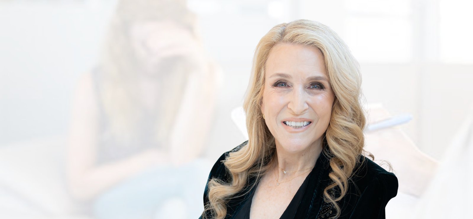 Smiling woman with long blonde hair against a soft blurred background.