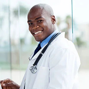 Smiling doctor in white coat with stethoscope around neck indoors.