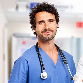Medical professional in blue scrubs with a stethoscope in a hospital corridor.