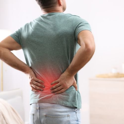 Man in green shirt holding lower back in pain at home.