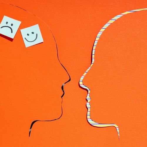Two face silhouettes with happy and sad sticky notes on orange background.