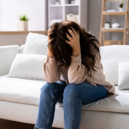 Woman sitting on a sofa with hands on her head.