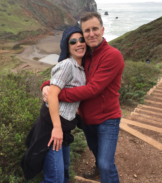 Couple smiling and hugging on a natural hillside landscape.